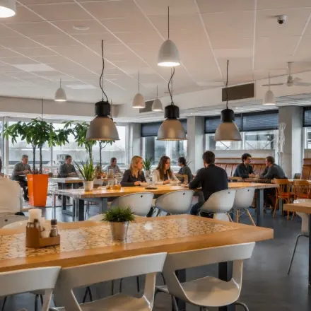 Bright, modern office space in Haarlem Waarderpolder with people working at communal tables, highlighting an open and collaborative environment ideal for office space rental.