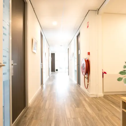 View of a well-lit hallway in an office space available for rent at Waarderweg 19, Haarlem Waarderpolder, featuring wooden flooring and framed prints on the walls.