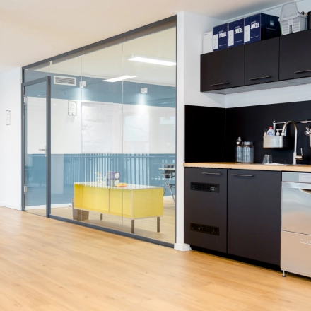 Contemporary furnished interior of an office with a kitchenette and glass-walled workspace at Versmannstraße 4, Hamburg Hafencity available for office space rental.