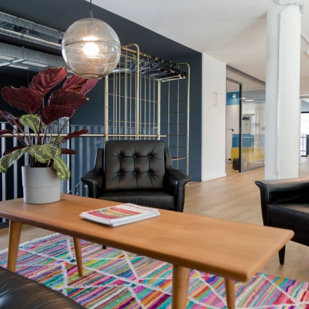 Furnished office space for rent at Versmannstraße 4, Hamburg Hafencity, featuring stylish black seating, a wooden coffee table, and a colorful rug under a modern light fixture.