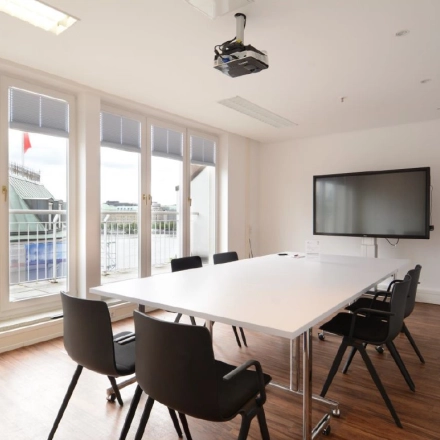 Bright office space with large windows, a table, chairs, and a TV, perfect for meetings. Ideal office space rental at Colonnaden 5, Hamburg Neustadt.