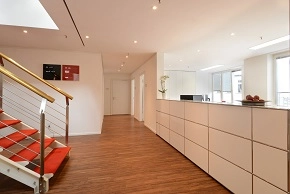 Bright office interior at Colonnaden 5, Hamburg Neustadt, featuring a modern reception area with wooden flooring and a staircase. Ideal office space rental for welcoming clients.