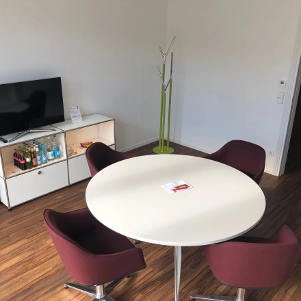 Cozy office space in Hamburg Neustadt with modern furnishings, including a round table and chairs, TV, and a small beverage shelf. Ideal for office space rental.