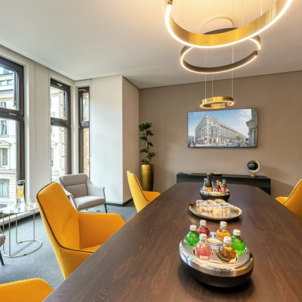 Bright office space on Alter Wall 32, Hamburg Old Town, featuring a large table, colorful chairs, and a city view. Ideal office space rental for meetings.