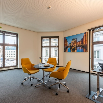 Well-lit office to rent at Alter Wall 32, Hamburg Old Town, featuring a small meeting area with chairs and desk, ideal for business discussions.