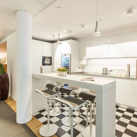 Modern office kitchen at Ballindamm 39, Hamburg Old Town, featuring a sleek white kitchenette with bar seating, ideal for breaks in an office space rental.