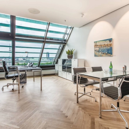 Bright office to rent at Ballindamm 39 with modern furnishings, featuring sleek desks and an impressive view through slanted windows, perfect for office space rental in Hamburg Old Town.