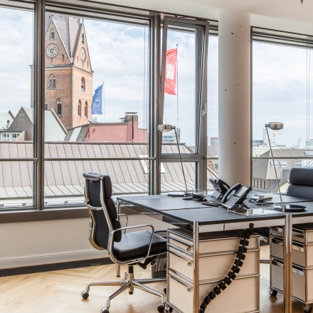 Bright office space for rent at Ballindamm 39, Hamburg Old Town. Features modern furnishings with desks and chairs, offering a city view.