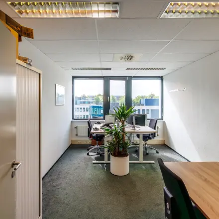 Interior view of an office space available for rent at Welbergweg 60, Hengelo, featuring desks, chairs, and natural light through large windows.