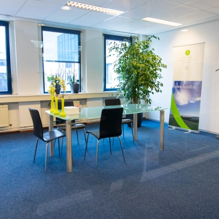 Bright office space to rent in Hilversum with large windows, a glass table surrounded by black chairs, and a coat rack.