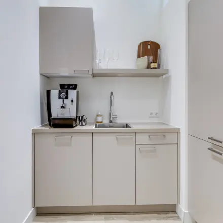 Compact kitchen area in an office space, featuring a coffee machine and storage cabinets. Ideal for office space rental opportunities.