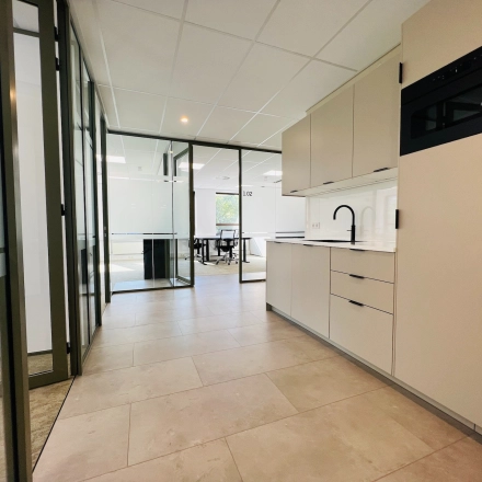 Modern office space available for rent in Hilversum's Marathon 2, featuring a sleek kitchenette beside spacious workspaces.