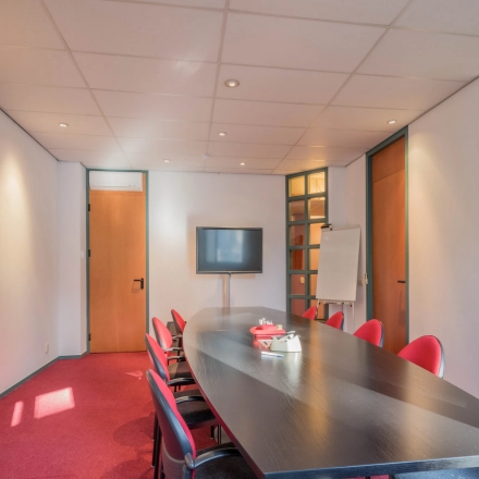 Office space for rent at Mozartlaan 27, Hilversum, featuring a conference room with a long table, red chairs, a TV, and a whiteboard.