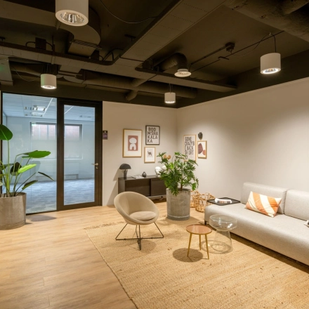 Stylish office space rental at Olympia 1, Hilversum with modern furnishings, a cozy seating area, and vibrant plants under soft lighting.