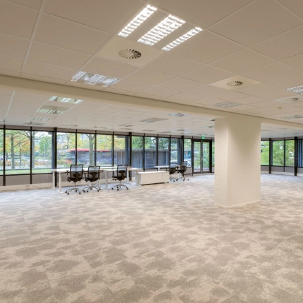 Interior view of an unfurnished office space for rent at Olympia 1, Hilversum, featuring large windows and ample floor area ideal for customization.