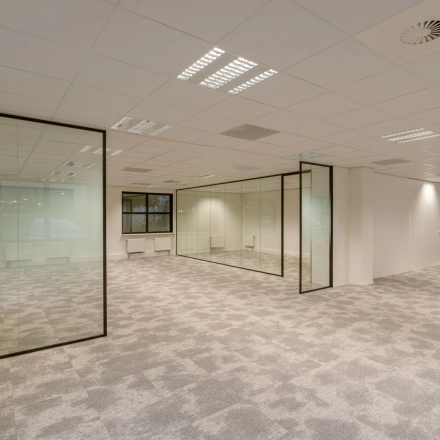 Spacious, unfurnished office for rent at Olympia 1, Hilversum featuring glass partitions and a carpeted floor.