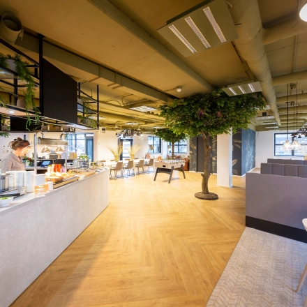 Spacious and modern workspace at Olympia 1, Hilversum, featuring a cafeteria area with a person serving refreshments and stylish furnishings perfect for office space rental.