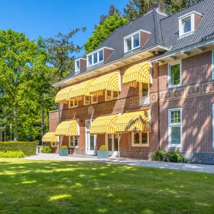 Exterior view of an office for rent at Utrechtseweg 47, Hilversum, featuring a traditional brick facade with yellow-striped awnings.
