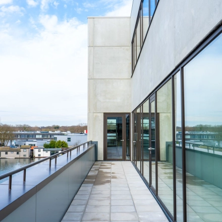 View of an office building's exterior at Zuiderloswal 55, Hilversum, highlighting large glass windows overlooking a waterfront. Ideal location for office space rental with modern architecture.