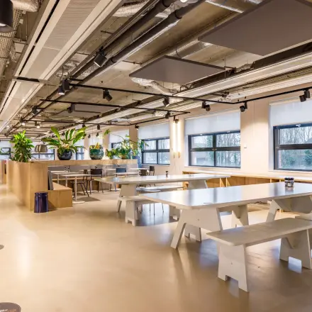Spacious and modern office interior at Siriusdreef 16, Hoofddorp, featuring furnished workspaces with tables, benches, and greenery. Ideal office space rental opportunity.