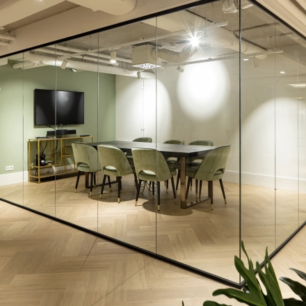 Modern conference room at Siriusdreef 60, Hoofddorp, featuring a large round table, green chairs, and a wall-mounted TV. Ideal office space rental for productive meetings.