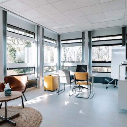Bright office space with modern furnishings available for rent at De Vos van Steenwijklaan 75, Hoogeveen. Features large windows, stylish chairs, and a meeting table, ideal for office space rental.