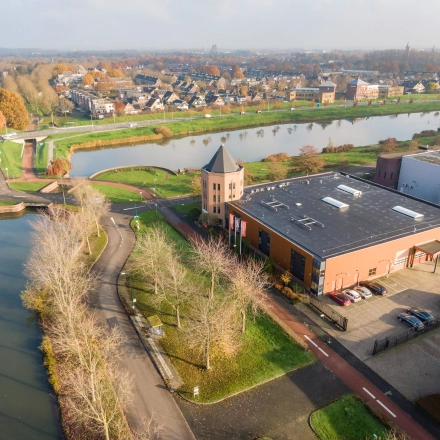 Aerial view of the office building at Hoofdveste 2, Houten, surrounded by a small canal and trees. The modern building offers office space rental in a scenic area with ample parking.