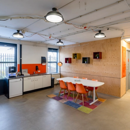 Modern office interior at Hoofdveste 2, Houten, featuring a bright multipurpose space with a meeting table and kitchenette. Ideal for office space rental in a vibrant, colorful setting.