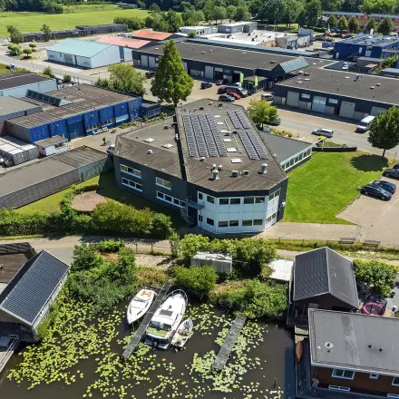 Overhead view of an office building at Ouddeelstraat 7a, Leeuwarden, surrounded by greenery and industrial buildings. Ideal for office space rental with ample parking opportunities.