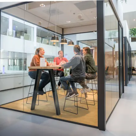 Modern office space rental at Bargelaan 200, Leiden, featuring a glass-enclosed meeting area with people engaged in discussion around a high table.