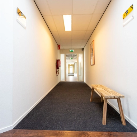 View of a well-lit hallway at Fruitweg 22, Leiden, featuring a wooden bench and bright walls, perfect for office space rental needs.