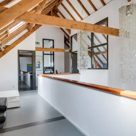 Interior of an office at Hamersveldseweg 120, Leusden, featuring wooden beams, modern furnishings, and decorative lighting. A sleek corridor connects different areas, ideal for office space rental.
