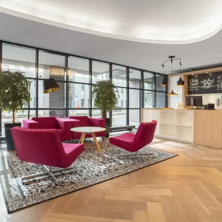 Spacious lobby area at Robert Schumandomein 2, Maastricht, featuring pink chairs, a front desk, and large windows. Ideal for businesses looking for office space rental.