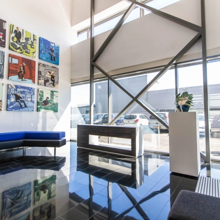 Bright office entrance with modern art on the wall, glass windows, and seating area. A person is walking outside. Ideal for office space rental.