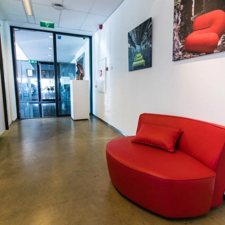 Spacious office entrance at Brieltjenspolder 28, Made, featuring a vibrant red couch and art on the walls, ideal for office space rental.