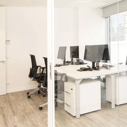 Bright office space with glass walls, featuring several desks and chairs in Madrid Azca.
