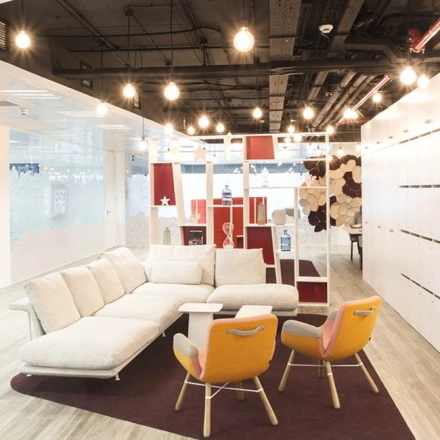 A spacious, modern office interior at Paseo de la Castellana 79, Madrid Azca, featuring contemporary furnishings including a comfortable sofa and stylish chairs under warm lighting.