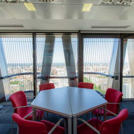 Modern office space with vibrant red chairs around a table, large windows providing a panoramic city view, ideal for office space rental.