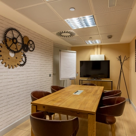 Interior of a furnished office space at Paseo de la Castellana 95 in Madrid Azca, featuring a table, chairs, and wall decor. A screen and flip chart suggest it's ideal for meetings.