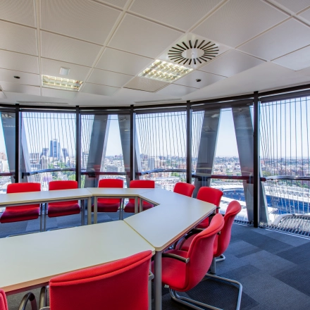 Bright office space for rent in Madrid Azca, featuring large windows with a stunning city view, and modern red and white furnishings arranged in a conference style.
