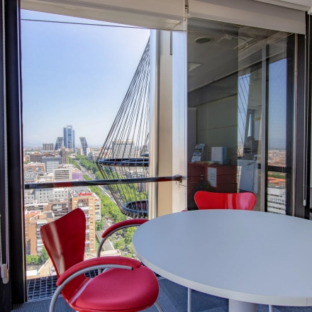 Office space for rent at Paseo de la Castellana 95, Madrid Azca, featuring a round white table and red chairs with a panoramic city view.