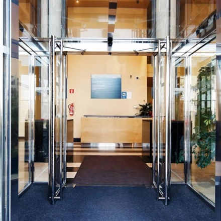 Entrance to a modern office space rental at Avenida de Aragón 334, Madrid Barajas, featuring glass doors and a reception desk.
