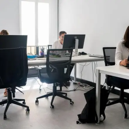 Professionals working at desks in a well-lit office at calle de las Huertas 11, ideal for office space rental in Madrid Center.