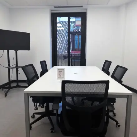 Compact office space rental at calle de las Huertas 11, Madrid Center, featuring a meeting table with chairs and a TV screen, ideal for collaborative work.