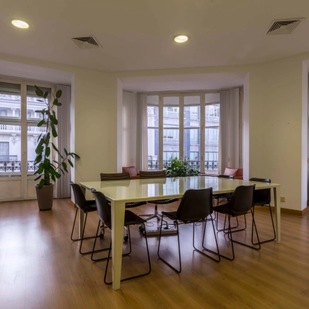 Spacious office to rent at Calle Gran Vía 6 in Madrid Center, featuring a modern meeting area with large windows, table, and chairs suitable for office space rental.