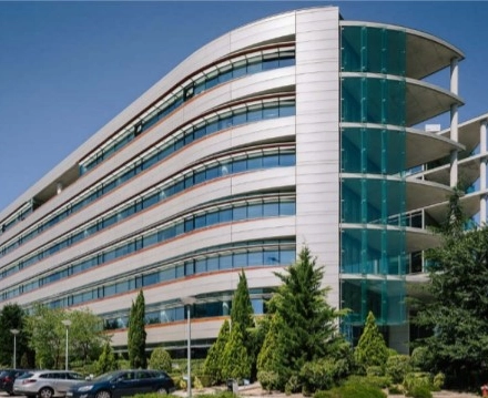 A modern office building at Calle Vía de los Poblados 1, Madrid Hortaleza, ideal for office space rental, surrounded by greenery and parking facilities.