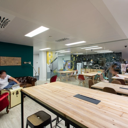 Shared office space to rent in Madrid Retiro, featuring long wooden tables, eclectic seating, and people collaborating in a vibrant setting. Ideal for office space rental.