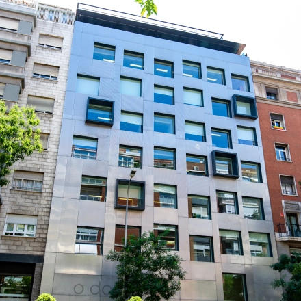 Modern exterior of an office building available for rent on calle de O'Donnell, Madrid Retiro, featuring geometric windows and surrounded by greenery.