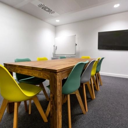 Modern office to rent in Madrid Retiro, featuring a wooden table with colorful chairs, whiteboard, and a screen, ideal for conferences or meetings.