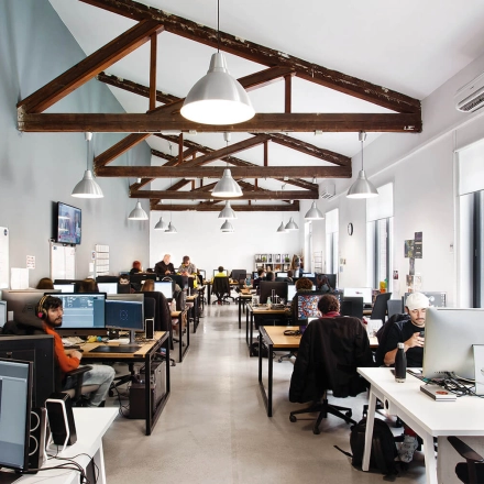 Modern office space in Madrid Retiro at Calle Vandergoten 1 with professionals working at computers under exposed wooden beams, ideal for office space rental.
